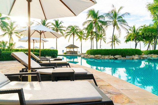 Guarda-chuva e cadeira ao redor da piscina em hotel resort para viagens de lazer e férias perto da praia do mar oceano