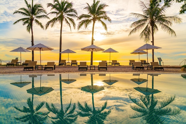 Guarda-chuva e cadeira ao redor da piscina no hotel resort para viagens de lazer e férias neary mar oceano praia ao pôr do sol ou nascer do sol