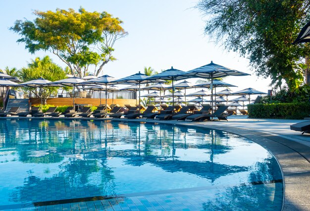 Guarda-chuva e cadeira de luxo bonito em torno da piscina no hotel e resort com céu azul