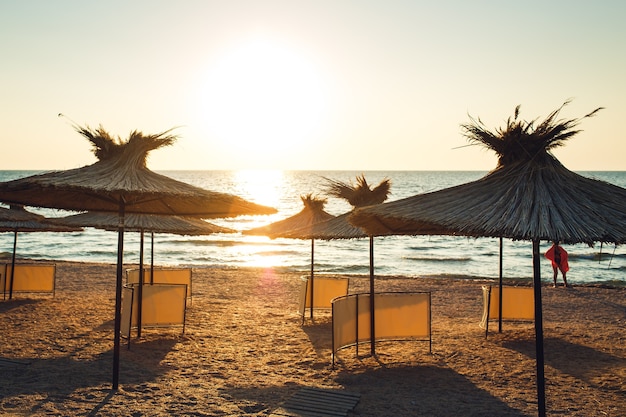 Guarda-sóis de junco da luz do sol da manhã na praia arenosa.