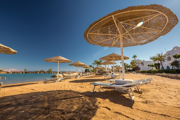 Guarda-sóis e espreguiçadeiras de palha na maravilhosa praia tropical