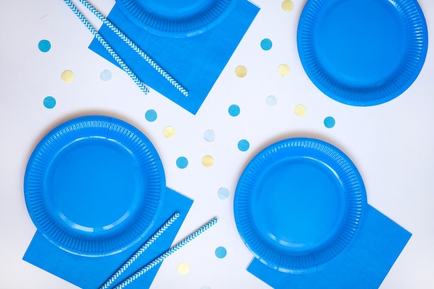 Guardanapos de pratos descartáveis de papel azul e canudos para bebidas na mesa de fundo branco