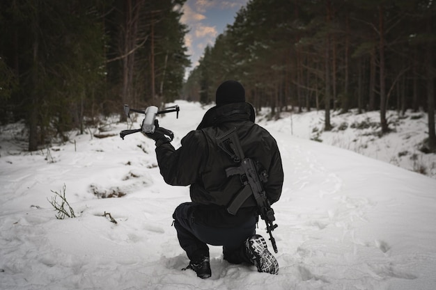 Foto un guardia fronterizo militar con un rifle detrás de su espalda lanza un dron en el bosque en invierno