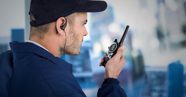 Foto guardia de seguridad con gorra y walkie talkie contra la ventana borrosa que muestra la ciudad