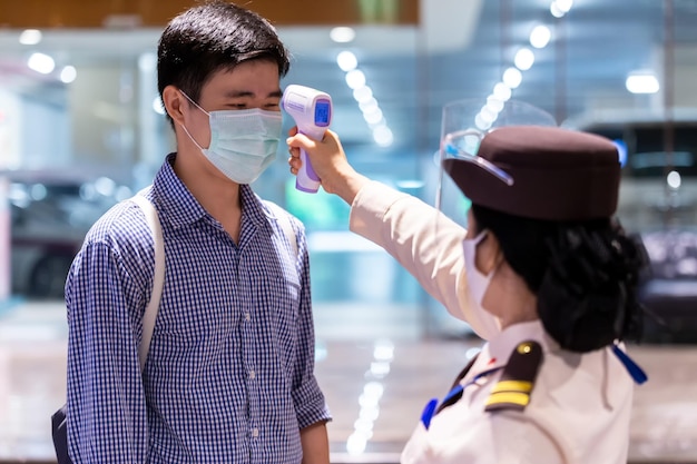 Foto guardia de seguridad que usa termómetro infrarrojo para medir la temperatura corporal verifica a las personas con máscara protectora