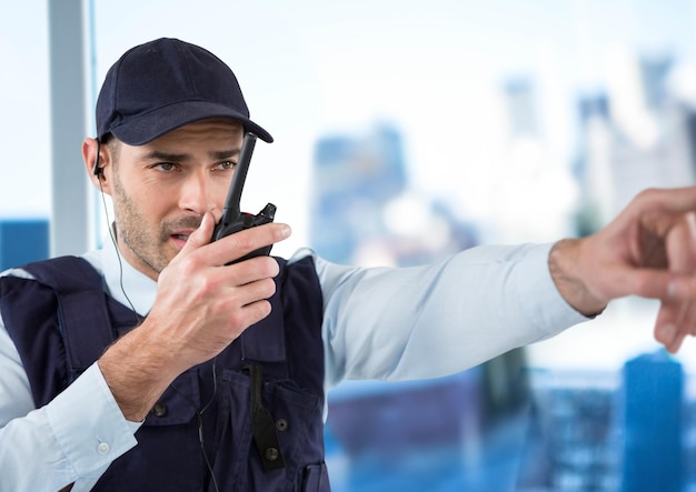 Guardia de seguridad con walkie talkie apuntando contra una ventana borrosa que muestra la ciudad