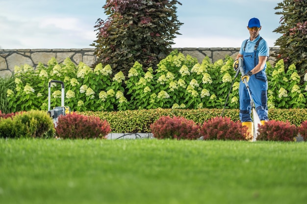 Guardián de jardín caucásico limpiando entrada residencial usando lavadora a presión profesional