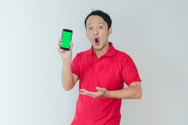 Guau cara de joven asiático sonriendo cuando muestra la pantalla verde del teléfono inteligente en el fondo del estudio