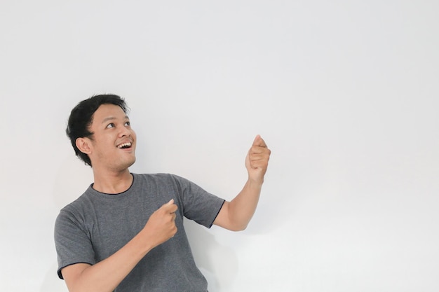Guau y cara sorprendida con una sonrisa de un joven asiático con una camiseta gris con un punto de mano en el espacio vacío