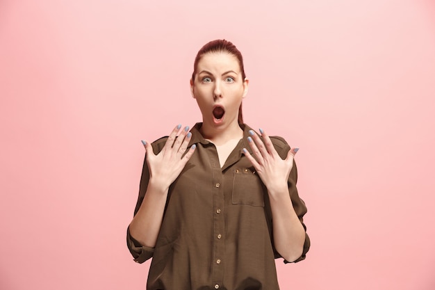 Guau. Hermoso retrato frontal de medio cuerpo femenino aislado sobre fondo de color rosa de estudio. Joven mujer emocional sorprendida de pie con la boca abierta. Las emociones humanas, el concepto de expresión facial. Colores de moda