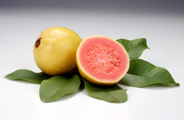 Guayabas divididas por la mitad y hojas sobre fondo blanco Frutas tropicales