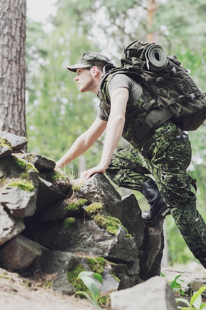 guerra, caminhadas, exército e conceito de pessoas - jovem soldado ou guarda florestal com mochila andando na floresta