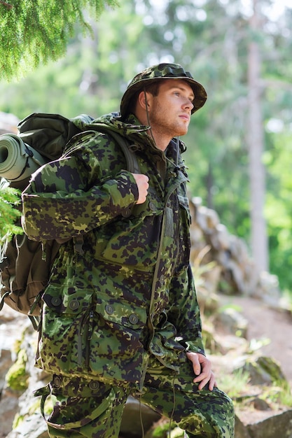 Foto guerra, caminhadas, exército e conceito de pessoas - jovem soldado ou guarda florestal com mochila andando na floresta