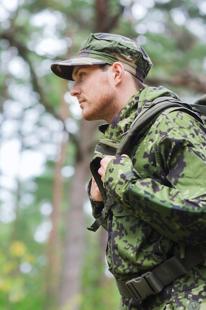 Foto guerra, caminhadas, exército e conceito de pessoas - jovem soldado ou guarda florestal com mochila andando na floresta