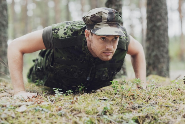 guerra, exército, treinamento e conceito de pessoas - jovem soldado ou ranger vestindo uniforme militar fazendo flexões na floresta