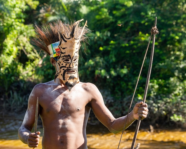 Guerreiro da tribo Asmat está de pé com uma máscara de batalha e um arco.