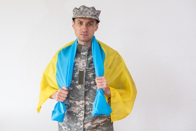 Guerreiro ucraniano vestido com um uniforme de pixel militar segura a bandeira azul-amarela do estado da Ucrânia e na corrente um pequeno brasão do país do tridente, close-up.