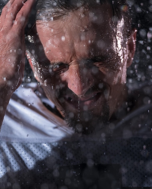 El guerrero atleta de fútbol americano parado en un campo sostiene su casco y está listo para jugar. Jugador preparándose para correr, atacar y anotar touchdown. Noche lluviosa con destello de lente dramático y gotas de lluvia. Alto