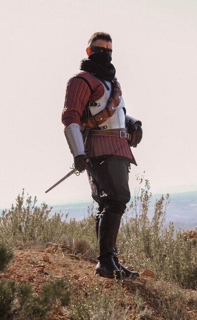 Foto guerrero medieval en el bosque, portando una espada y una antorcha.