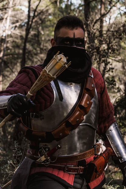 Foto guerrero medieval en el bosque, portando una espada y una antorcha.