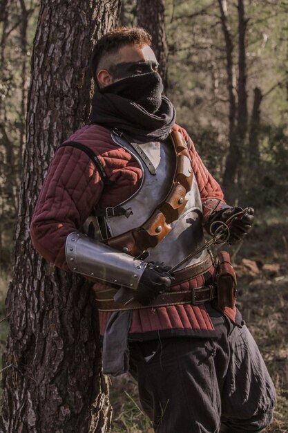 Foto guerrero medieval en el bosque, portando una espada y una antorcha.