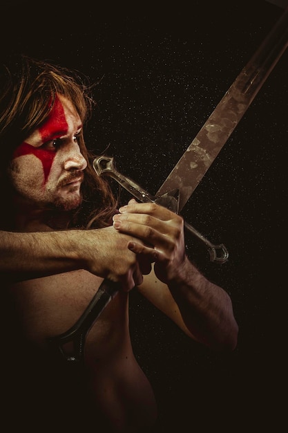 Guerrero salvaje con espada de metal y pinturas de guerra en la cara, cabello largo