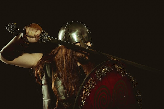 Guerrero vikingo con casco metálico y pieles de animales. guanteletes de cuero, escudo de madera rojo con adornos dorados y espada de acero