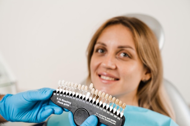 Guia de tons de cor dos dentes com paciente mulher Clareamento dental Dentista trabalhando com amostras de correspondência de cores dos dentes na clínica odontológica Odontologia