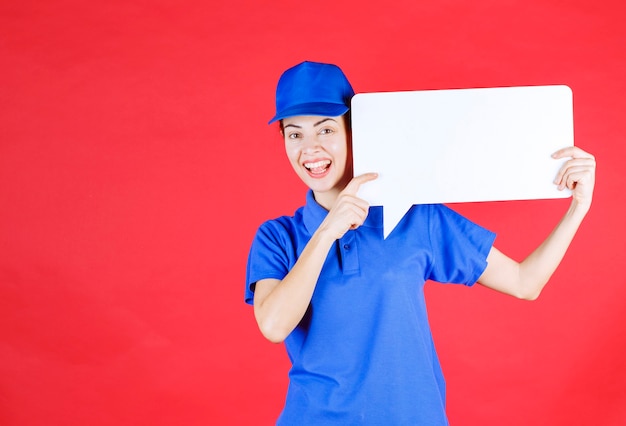 Guía femenina en uniforme azul sosteniendo un tablero de información rectangular blanco.