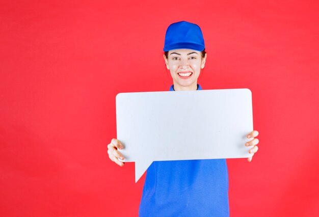 Guía femenina en uniforme azul sosteniendo un tablero de información rectangular blanco.