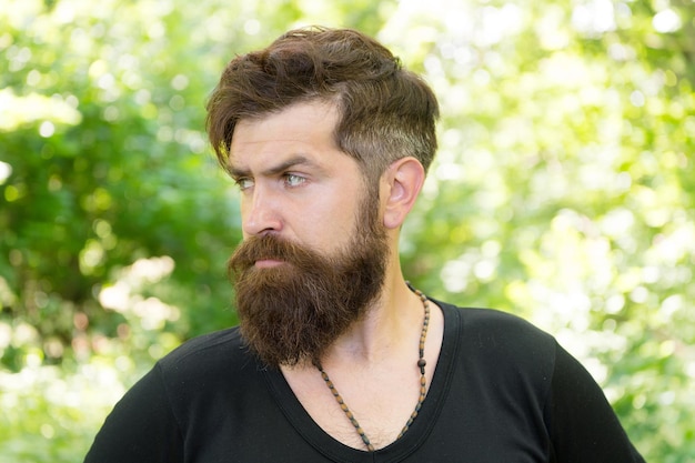 Guía de supervivencia en la naturaleza. Hombre barbudo fondo de follaje brillante hipster. Guy relajarse en el bosque de verano. Hombre guapo con barba y bigote vacaciones de verano. Concepto de temporada de calor de verano. Cuidado facial.