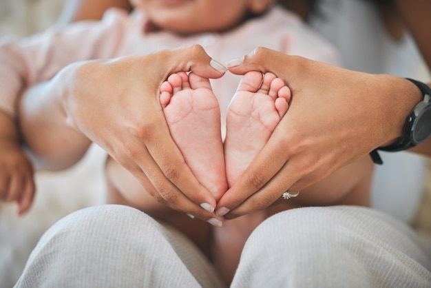 Guiando con amor. Captura recortada de las manos de una mujer irreconocible formando un corazón alrededor de los pies de su bebé recién nacido en casa.