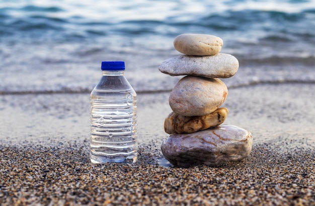 guijarros en una botella de agua de plástico piramidal o una taza de café en la playa del mar.