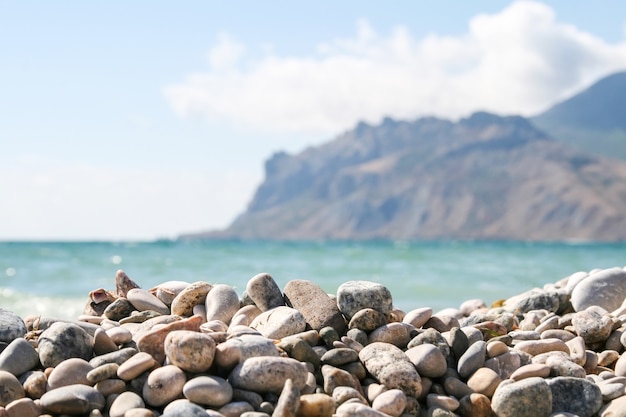 Guijarros de mar contra las montañas borrosas y el mar