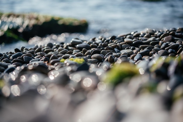 Guijarros de playa con chispas de sol y olas de mar espumosas