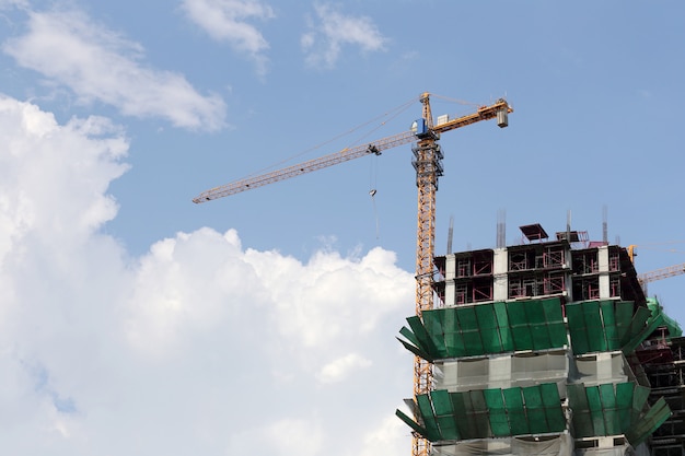 Guindaste que trabalha em um edifício sob a construção no tempo do dia.