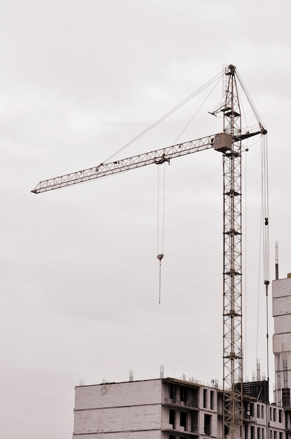 Guindastes altos de trabalho dentro do lugar para com construções altas sob a construção contra um céu azul claro.