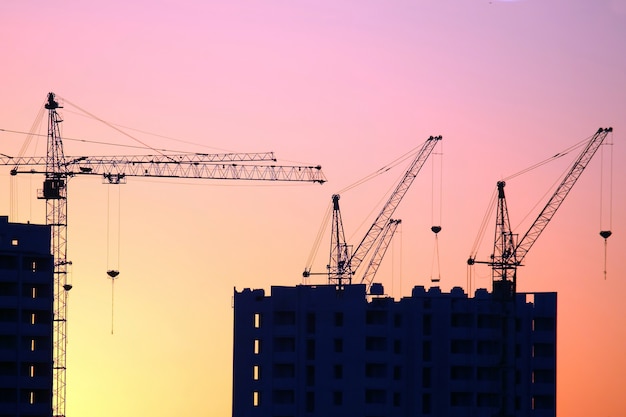 Guindastes de construção com casas construídas no fundo do céu do sol. indústria de construção industrial