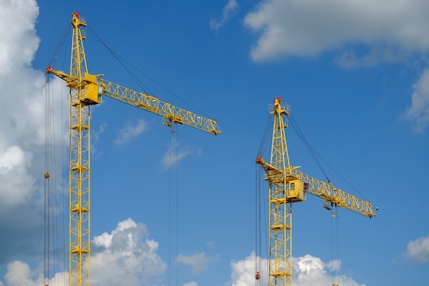 Guindastes de construção e construção de casa contra o céu azul