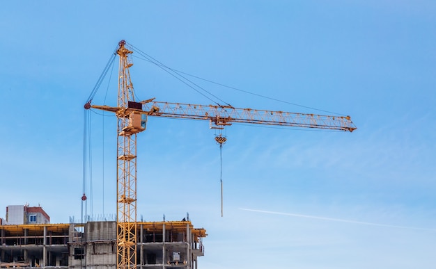 Guindastes de construção e prédio de apartamentos inacabado contra o céu azul. Construção de moradias.