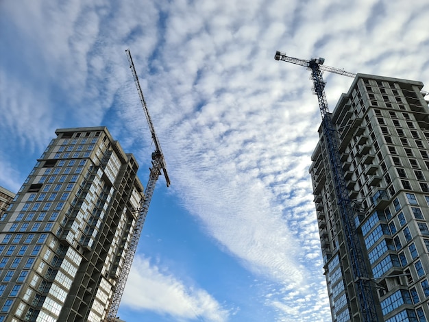 Guindastes de construção perto de edifícios de vários andares contra o céu azul