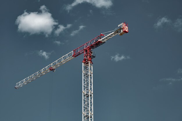 Guindastes de construção trabalham no local de criação contra o fundo do céu azul. Vista inferior do guindaste industrial. Conceito de construção de prédios de apartamentos e renovação de habitações. Copie o espaço