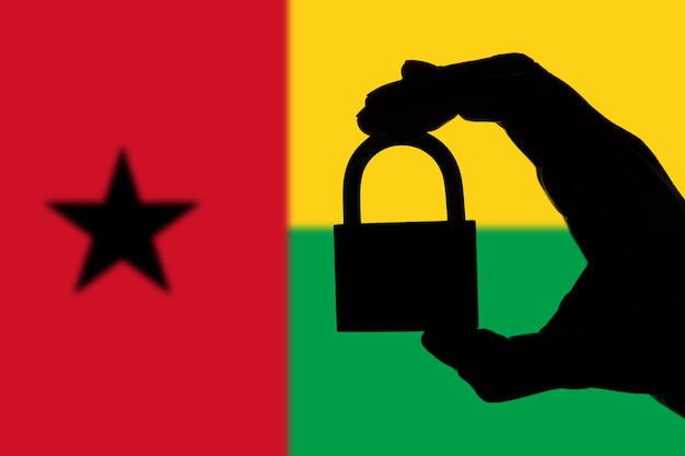 Guinea-Bissau-Sicherheit Silhouette einer Hand, die ein Vorhängeschloss über der Nationalflagge hält