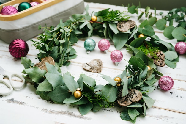 Guirlanda de eucalipto verde, decorações de Natal e enfeites na mesa de madeira branca