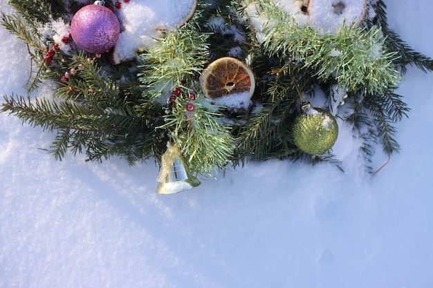 Guirlanda de Natal decorada com fatias de laranja secas e bolas coloridas em fundo branco de neve.