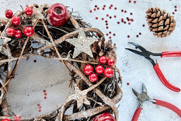 Guirlanda de natal feita de ramos decorados com estrelas douradas de madeira e bolhas vermelhas de frutas vermelhas. hobby de artesanato criativo. fazendo decorações de natal artesanais. aula de vista superior com alicate de metal, pinças