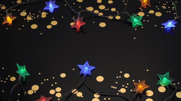 Foto guirlanda em forma de estrelas doces douradas em um fundo preto decoração de natal lanternas