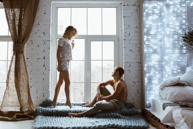 Guirlandas de ano novo a brilhar. casal perto da janela. Pijama cinza em corações. História de amor.