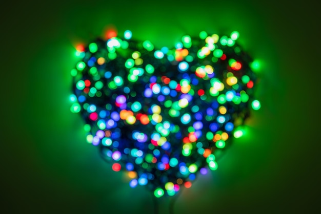 Guirnalda borrosa con luces multicolores dobladas en forma de corazón sobre un fondo verde