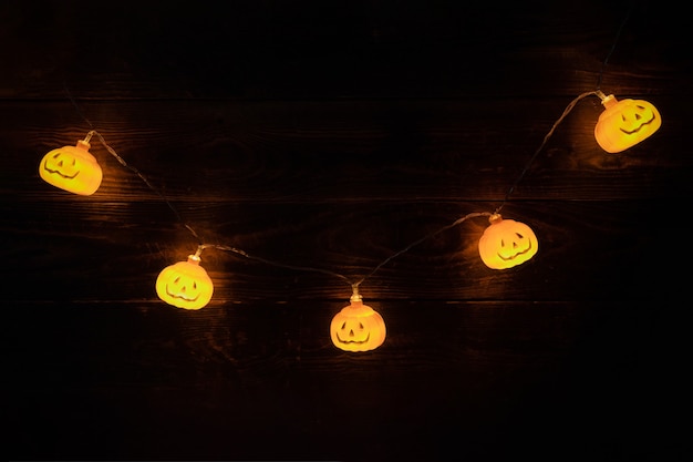 Guirnalda brillante con lámparas de calabaza de halloween sobre fondo de madera oscura.